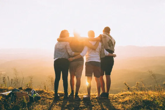 Group of four people with back to camera hugging and looking into sunset