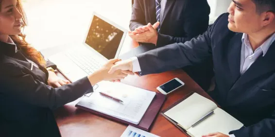 Woman and man shaking hands above desk.