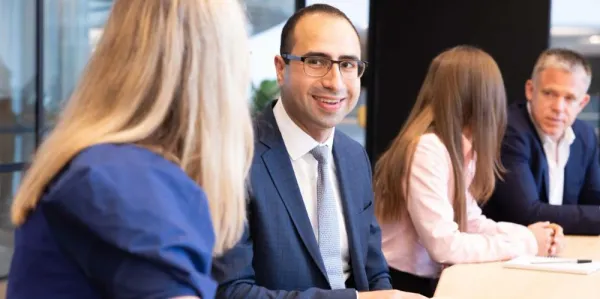 Man in meeting, smiling at female colleague.