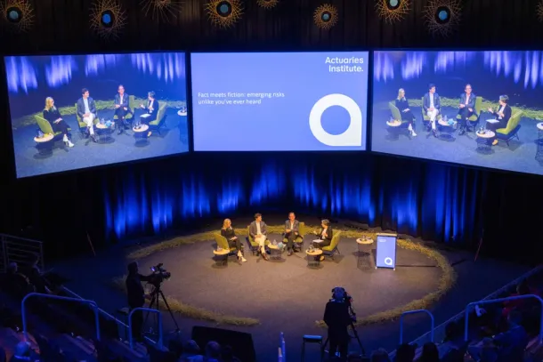 Photo from the All Actuaries Summit Gold Coast, with four presenters in the center stage, and three massive screens above them