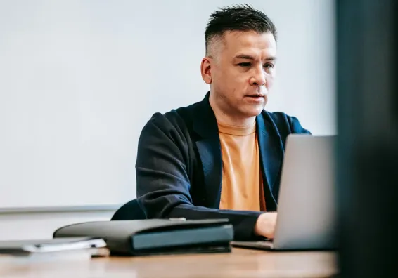 Man in orange shirt and suit jacket typing on a laptop