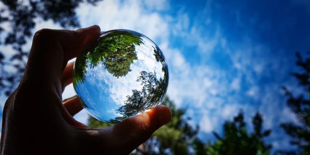 Person holding a viewfinder against nature and blue sky.