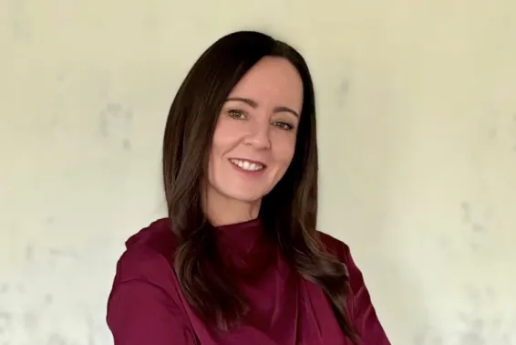 Woman looking at camera smiling with brown hair to shoulders and maroon silk top.