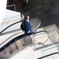 Man in blue business suit with black back pack and headphones walking at the top of escalator