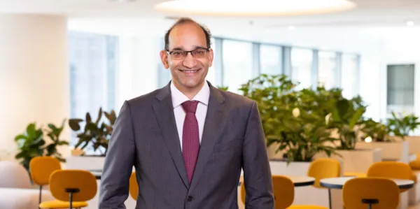 Business man in grey business suit and mauve tie in office with yellow chairs in background