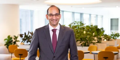Business man in grey business suit and mauve tie in office with yellow chairs in background