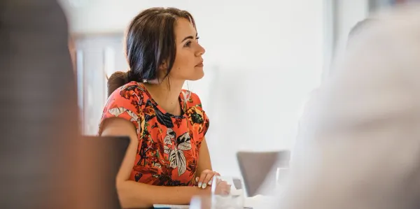 Woman sitting at a desk wearing orange listening in a meeting