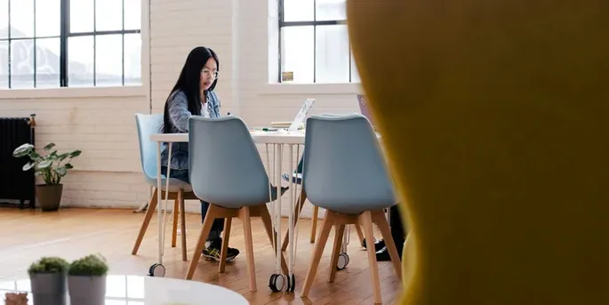 Woman with black hair sitting at a desk working on a laptop