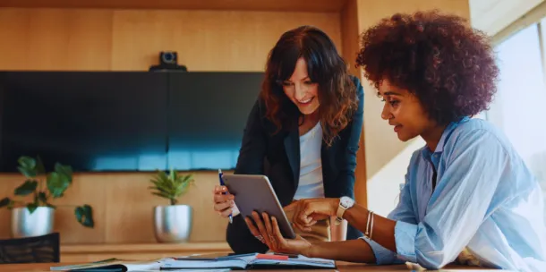 Two professional women look at tablet computer in an office