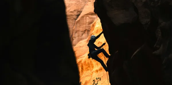 A photo of a person rock-climbing a red and orange cliff. They are wearing appropriate safety gear. 