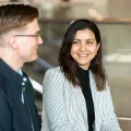 A man with glasses and a woman with brown hair and a striped blazer talking at event