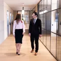 Business women and man walking down office corridor with glass fronted offices in background