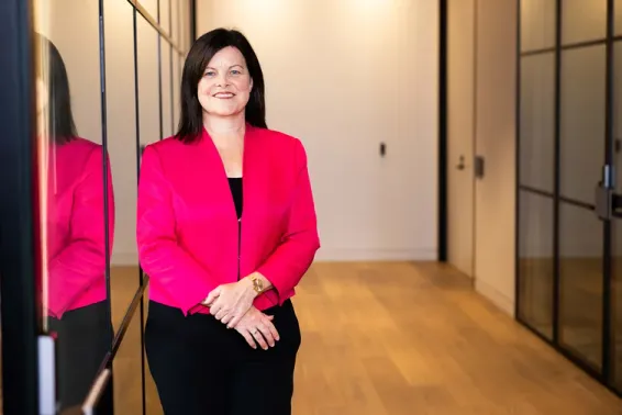 Actuary with brown hair and a pink jacket standing next to a door