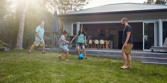 Two dads and two kids playing with a soccer ball in a backyard.