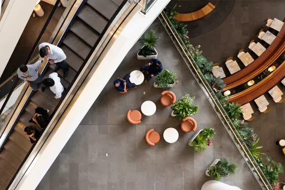 Two people going down an escalator and birds eye shot of a building with chairs and plants