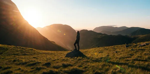 Person standing on a hill beneath mountains at sunrise