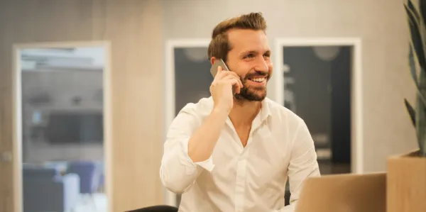 Business man smiling and talking on the phone, in a white shirt.