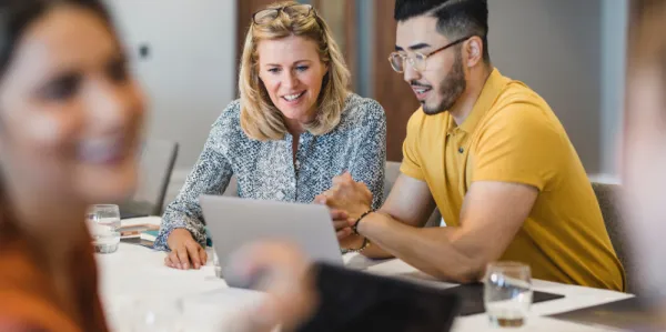 Two professionals - one man and one women - collaborating together on a laptop. 