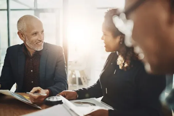 Two people meeting at conference table. Light streaming in window behind.