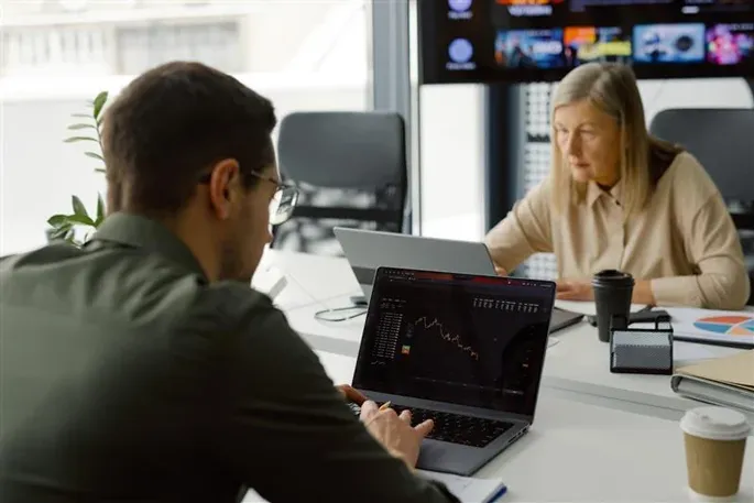 Two people typing at a desk looking at graphs