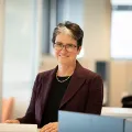 Business woman smiling and sitting at desk with burgandy suit
