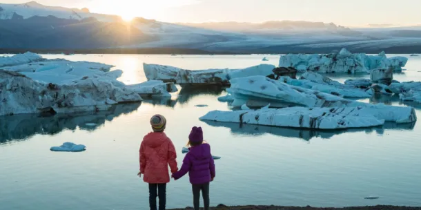 Children holding hands watching the sun rise over an icy terrain