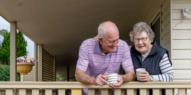 Elderly couple on the porch of their house, enjoying a hot beverage together whilst sharing a laugh