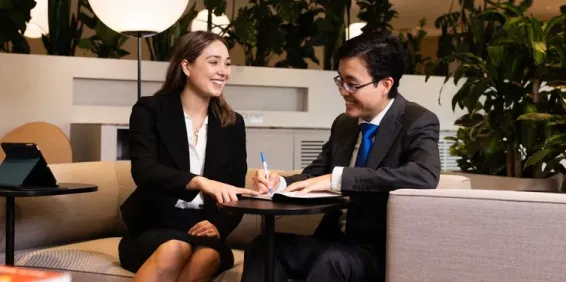 Professional man and woman sitting on lounge, writing notes in notebook.