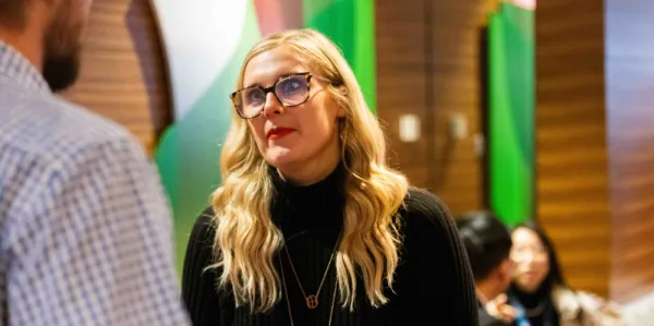 Female with glasses, long blonde hair and black polo jumper at a conference