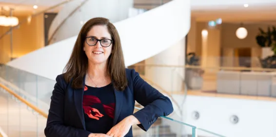 women with brown hair and glasses smiling and leaning on glass bannister in office foyer