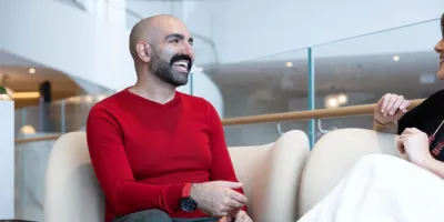 Man sitting on lounge smiling with red jumper and talking to work colleague