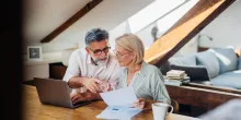 Senior couple sitting at a desk in their home office, working on documents together using a laptop