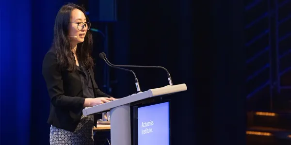 Jess Chen wearing black blazer on stage speaking at Actuaries Institute event.