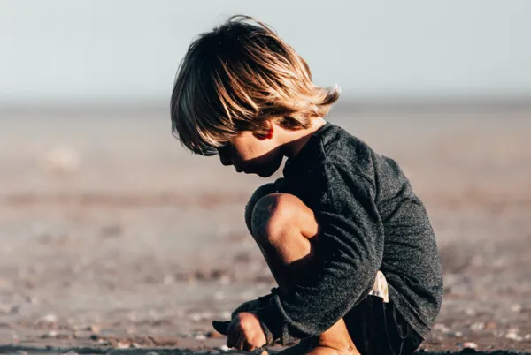 Young boy crouching in the sand.