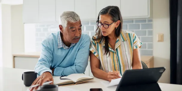 An elderly couple is sitting at their kitchen counter reviewing their finances.