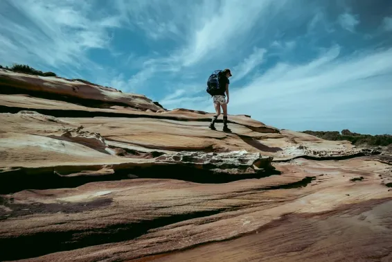 A lone hiker wearing a backpack hiking across Australian rocks