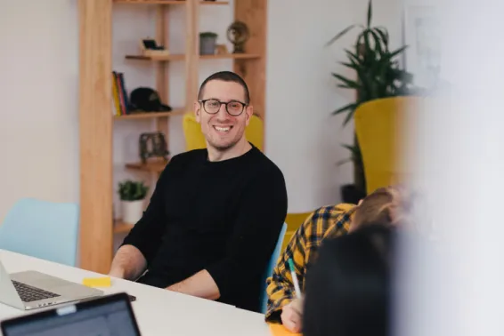 Man with glasses and black short sitting at a table, looking to slide and smiling