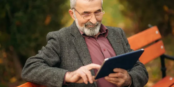 Man sitting on bench looking at a tablet computer.