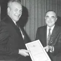 A black and white photo of two professional men holding out a certificate and smiling.