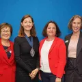 Four professional women stand smiling at the camera.