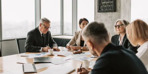 Men and women in business attire sit at a boardroom table.