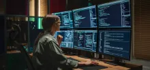 Women working at a desk with multiple screens showing coding.