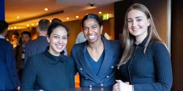 Three women at a conference, smiling looking at camera, with navy business outfits