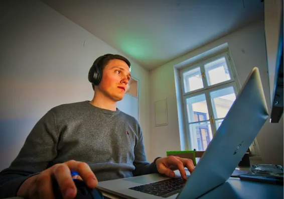 A mid-20s man with headphones on, working on his laptop. 