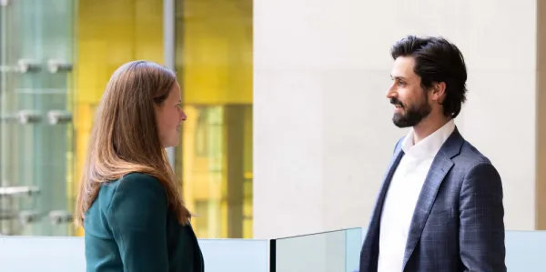 Man in suit and woman in green jacket standing in a foyer talking