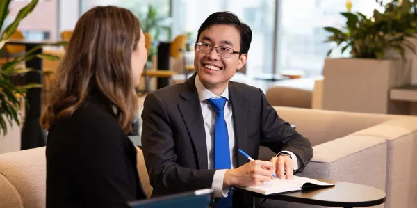 Woman with brown hair and man with black hair and blue tie sitting at a table working together