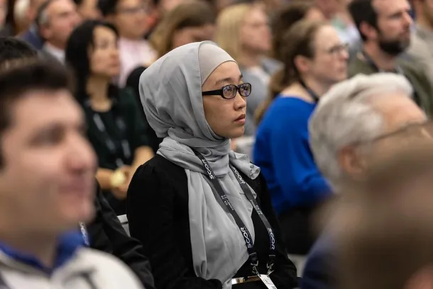 Photo of a seminar or session where hundreds of people are listening intently, the focus of the photo is on a woman in the sea of listeners
