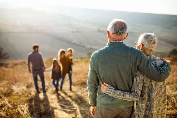 Back view of embraced grandparents enjoying while looking at their family on a field in autumn day.