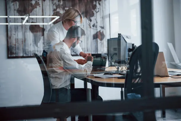 View through the glass. Two stockbrokers in formal clothes works in the office collaborating on a project.