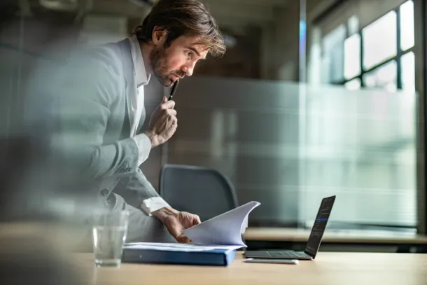 Worker comparing documents with computer data while sitting on a desk in the office.